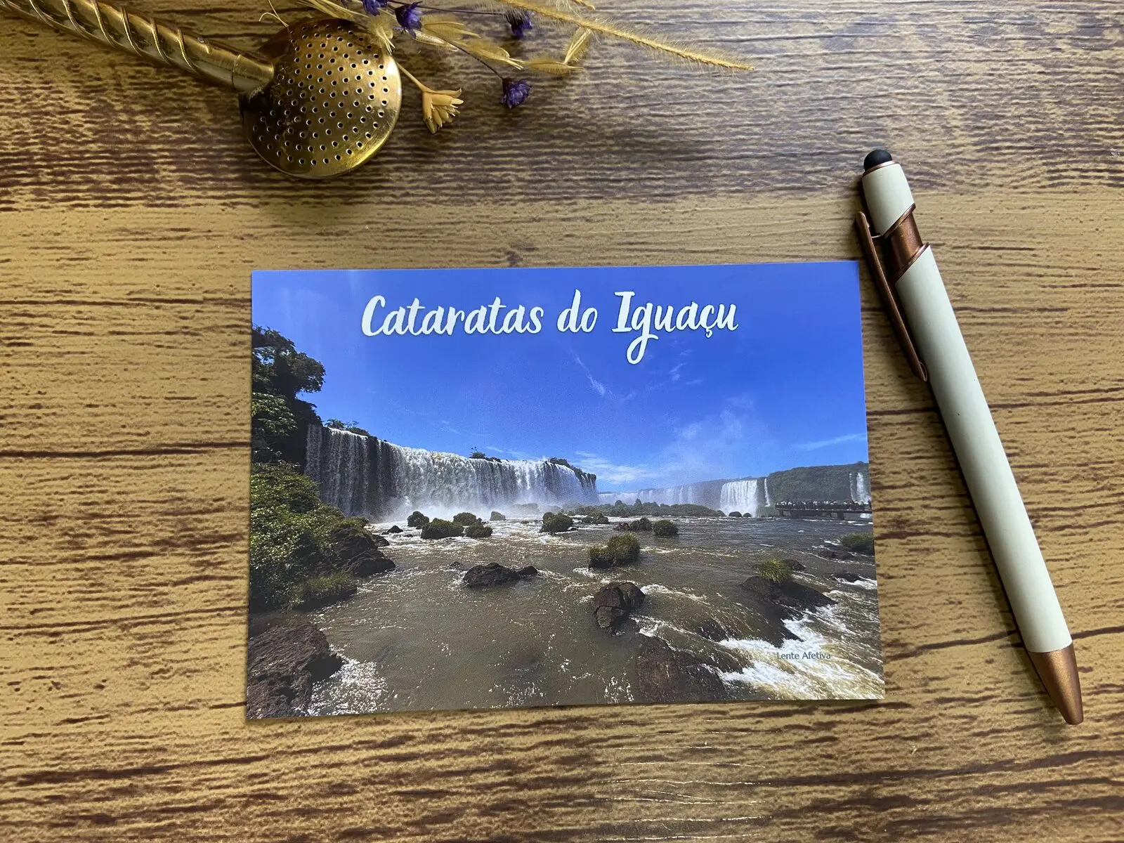 Cartão postal das Cataratas do Iguaçu sobre mesa, com caneta e infusor